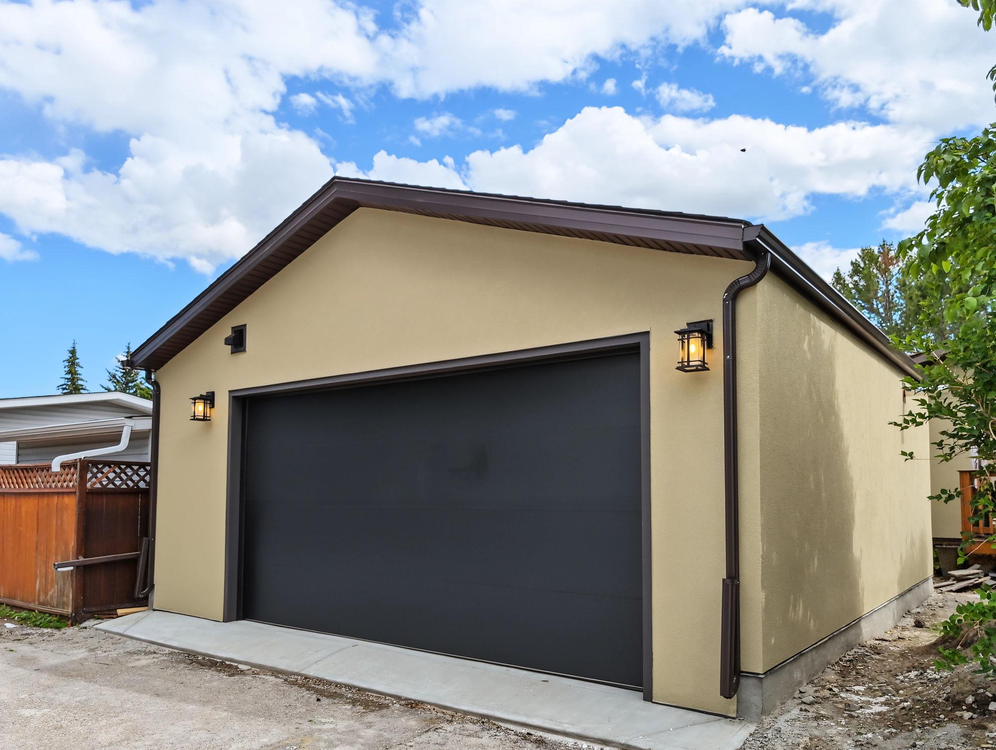 Finished stucco garage in Braeside with a black flush-panel overhead door and a lantern each side