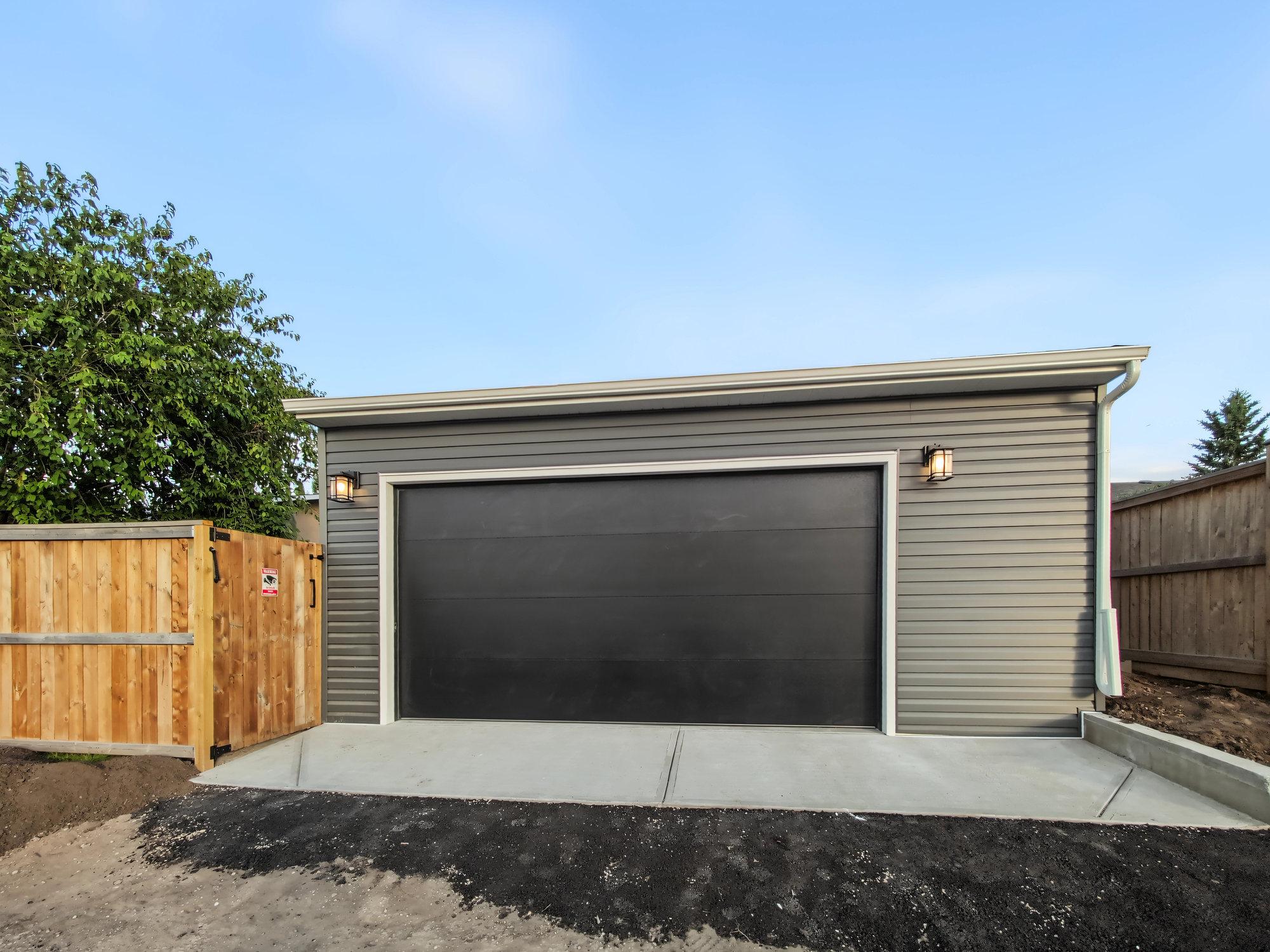 Finished garage in Maple Ridge in dark grey vinyl siding with a black overhead door in white trim
