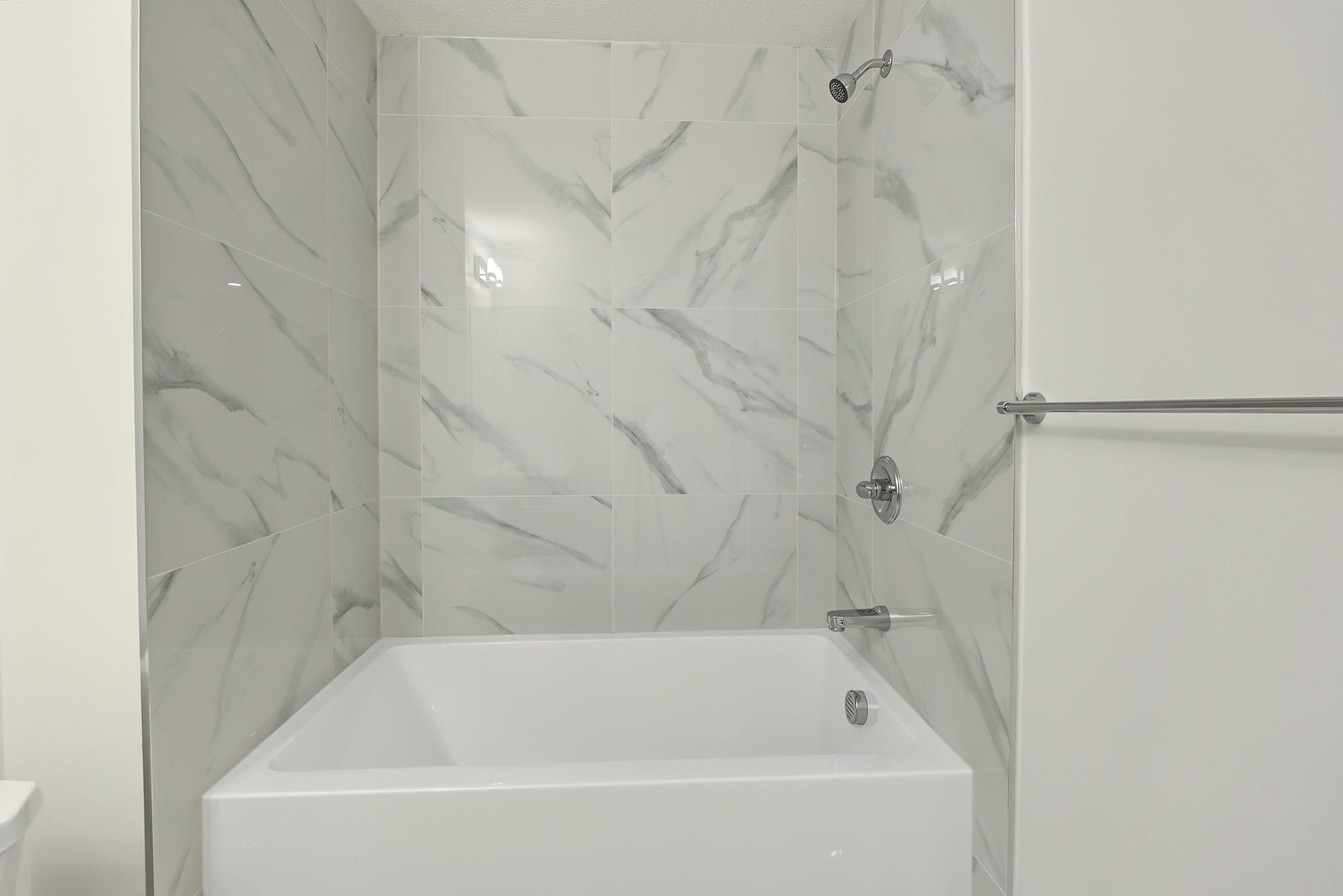 Alcove tub with marble-look tile to the ceiling and a chrome shower set