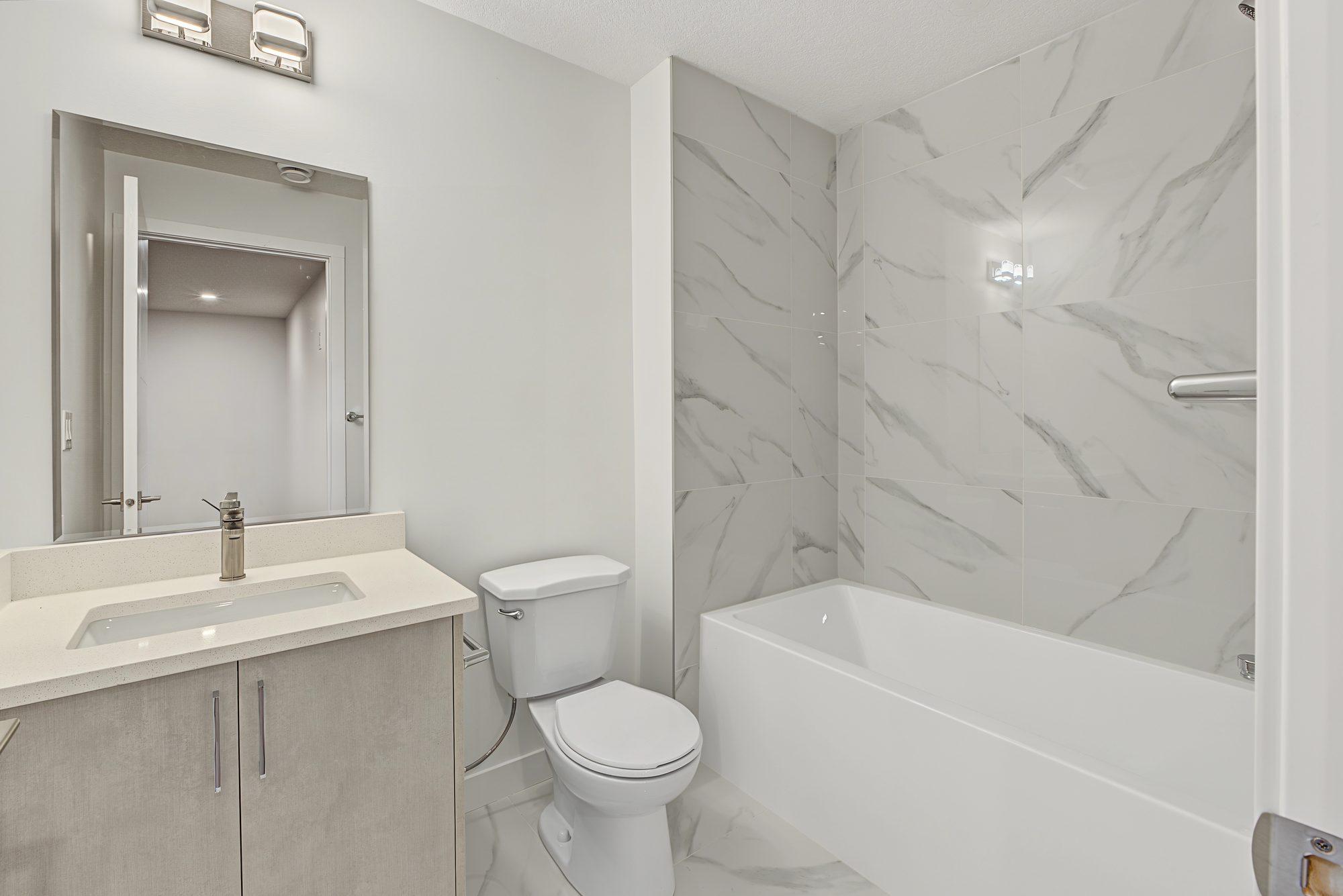 4-piece bathroom: vanity with quartz top and mirror, toilet, and a tub with marble-look tile to the ceiling