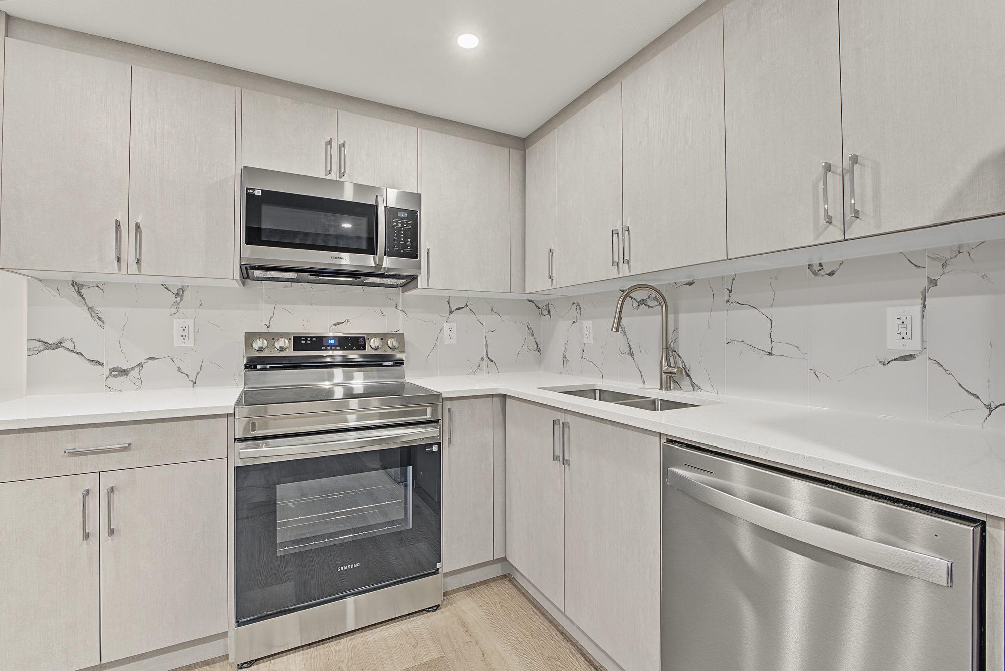L-shaped suite kitchen: quartz counter, marble-look 12 by 24 tile backsplash, stainless range, microwave hood and dishwasher