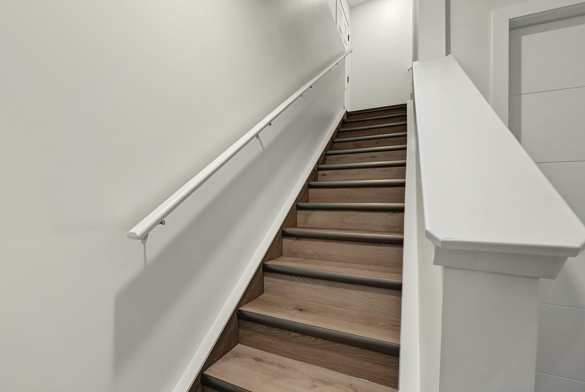 The suite's own stairs down from the separate entrance, vinyl plank treads with metal nosings