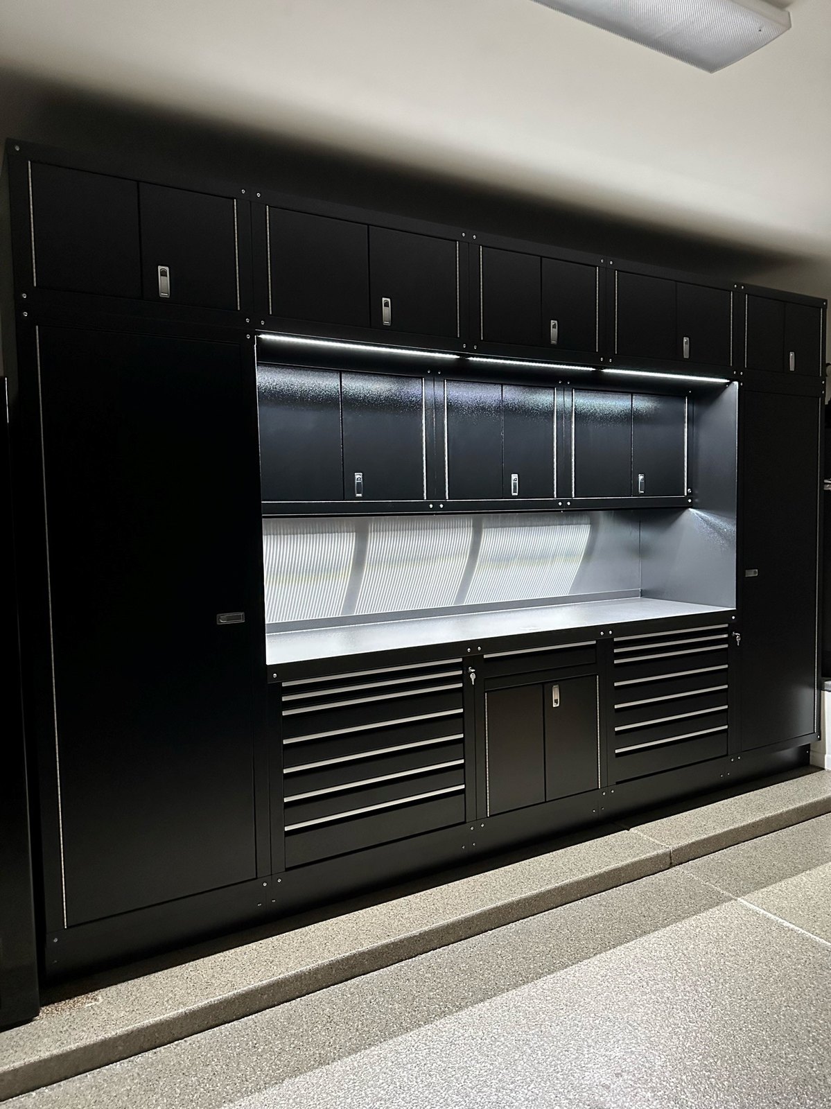 Black Cabinets by Hayley wall, installed: two full-height closets, upper cabinets with an LED strip, drawer stacks and a tool chest on a grey flake floor
