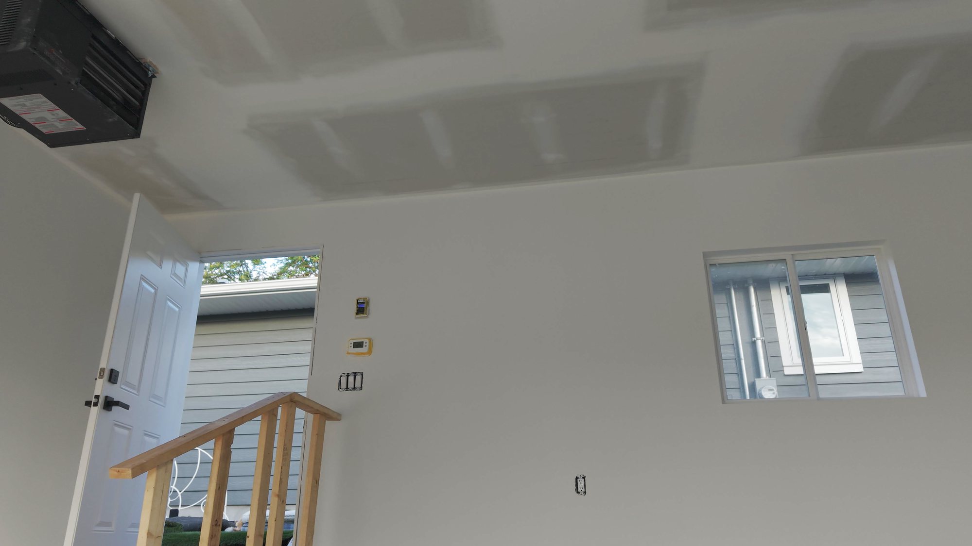 Garage interior with the drywall joints mudded flat and ready for primer, the gas unit heater hung at the ceiling and steps up to the man door