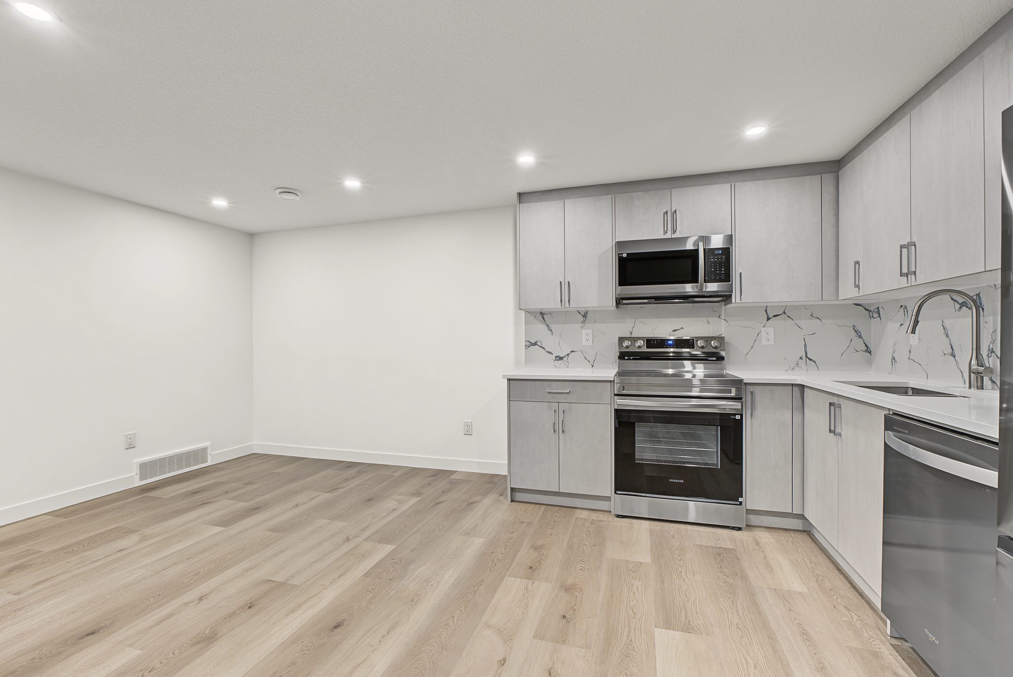 Suite living room with light oak vinyl plank floor, pot lights and the kitchen beyond