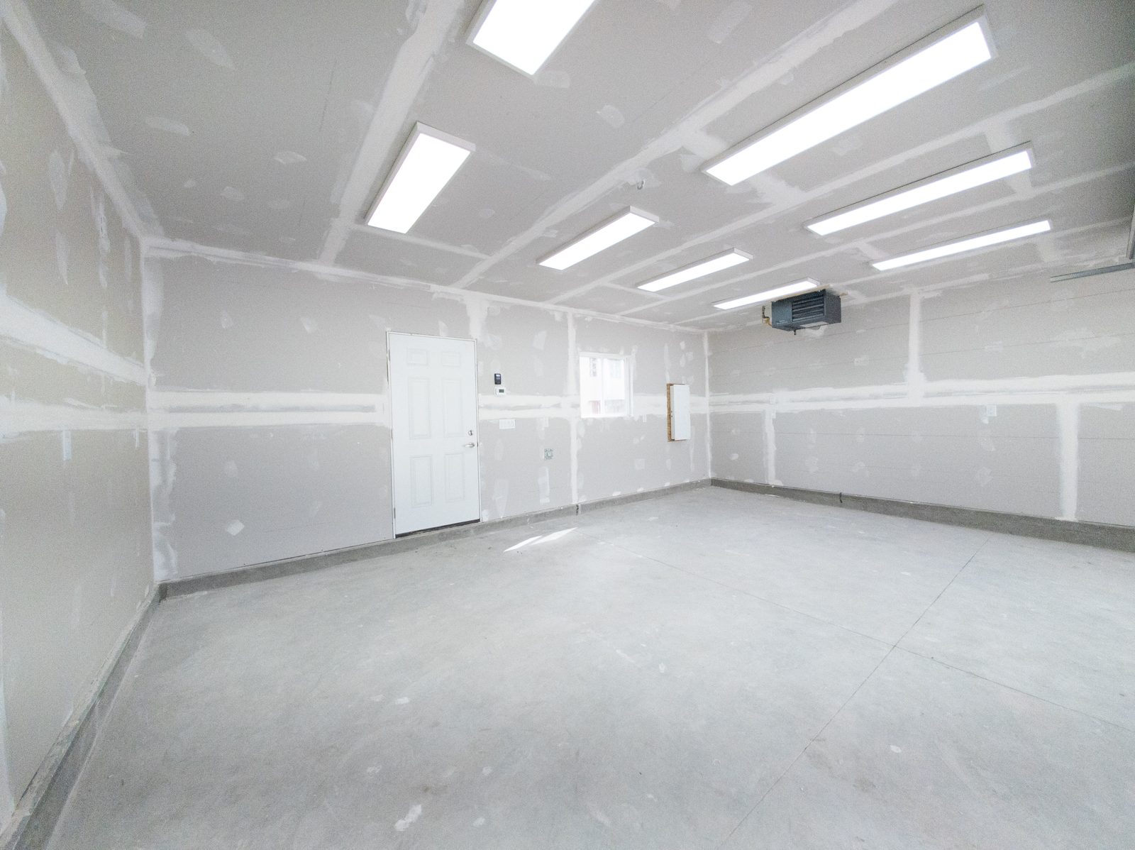Garage interior with the drywall hung and the first coat of tape on the joints, LED strip lights and a unit heater on the ceiling
